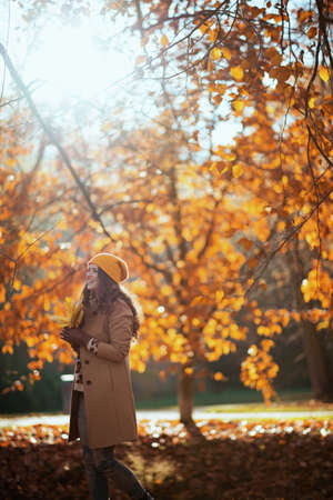 Hello september. happy trendy woman in brown coat and yellow hat having fun time outdoors in the city park in autumn.の写真素材