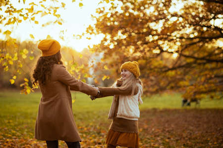 Hello autumn. happy young mother and daughter in orange hats with autumn yellow leaves outside on the city park in autumn.の写真素材