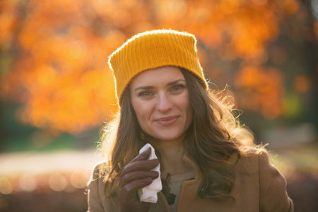 Hello october. smiling stylish 40 years old woman in brown coat and yellow hat among autumnal foliage outdoors on the city park in autumn.の写真素材
