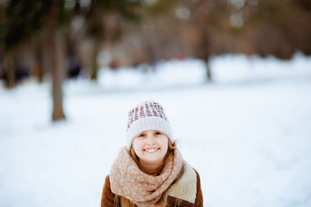 stylish girl with mittens in a knitted hat and sheepskin coat playing outside in the city park in winter.の写真素材