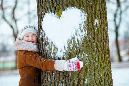 stylish girl with mittens in a knitted hat and sheepskin coat playing outside in the city park in winter.の写真素材