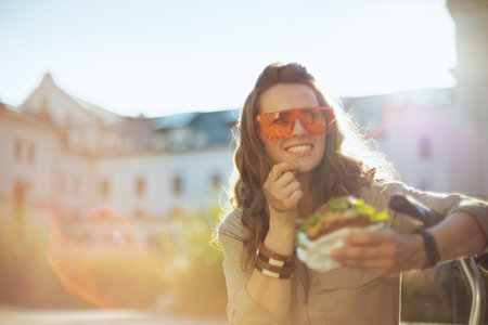 happy trendy woman in overall with string bag against black wood wall outdoors in the city.の写真素材