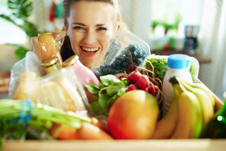 Food delivery. Closeup on smiling middle aged woman with food box in the kitchen.の写真素材