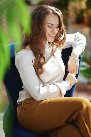 Green Home. happy modern housewife with long wavy hair in the modern living room in sunny day in beige pants and blouse.の写真素材