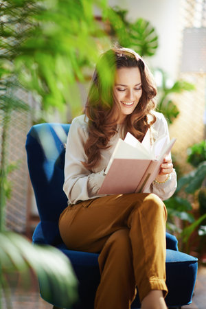 Green Home. happy modern housewife with long wavy hair in the modern living room in sunny day in beige pants and blouse.の写真素材