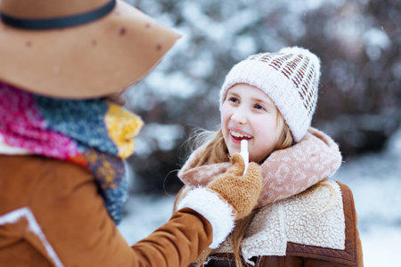 happy modern mother and child in hats and sheepskin coats disinfecting hands with an antibacterial agent outdoors in the city park in winter.の写真素材