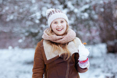 happy modern girl in a knitted hat and sheepskin coat with mittens playing outside in the city park in winter.の写真素材