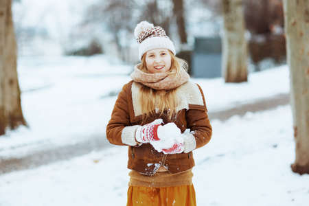 happy modern girl in a knitted hat and sheepskin coat with mittens playing outside in the city park in winter.の写真素材