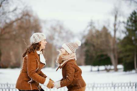 happy stylish mother and child in a knitted hats and sheepskin coats with mittens and medical mask in a knitted hat and sheepskin coat outdoors in the city park in winter.の写真素材