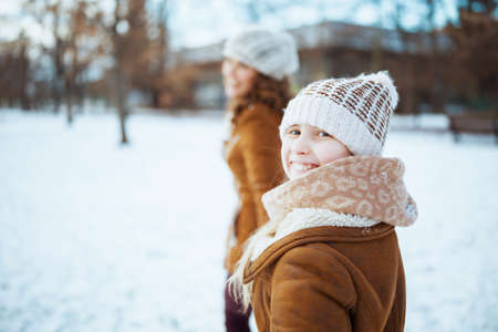 happy stylish mother and child in a knitted hats and sheepskin coats with mittens and medical mask in a knitted hat and sheepskin coat outdoors in the city park in winter.の写真素材