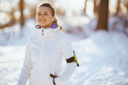 Full length portrait of young woman in white jacket workout outside in the city park in winter.の写真素材