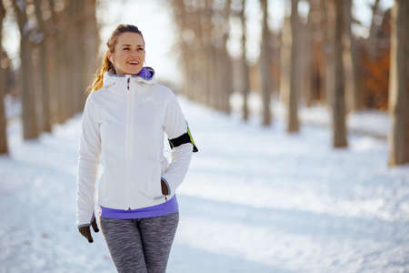 Full length portrait of young woman in white jacket workout outside in the city park in winter.の写真素材