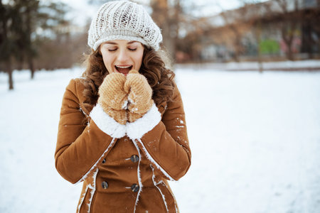 Portrait of happy modern 40 years old woman with mittens and cup of cappuccino in a knitted hat and...