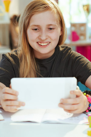 smiling modern school girl in grey shirt with tablet PC having distance education at home in sunny day.の写真素材