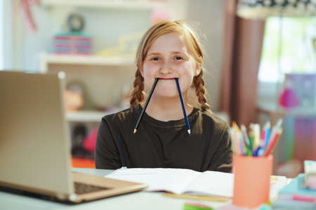 bored modern girl in grey shirt with laptop and workbook homeschooling and fooling around at home in sunny day.の写真素材