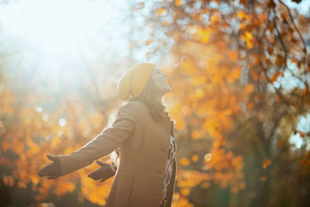 Hello autumn. happy stylish woman in brown coat and yellow hat with autumn yellow leaves outside in the city park in autumn.の写真素材