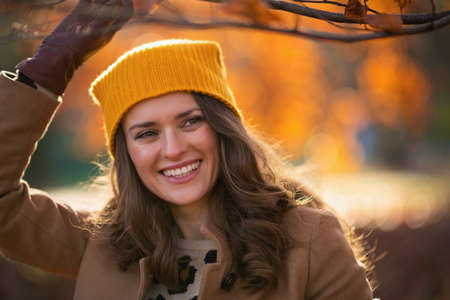 Hello autumn. happy stylish woman in brown coat and yellow hat with autumn yellow leaves outside in the city park in autumn.の写真素材