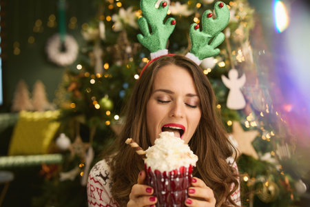Christmas time. Closeup on happy middle aged woman with Santa hat in traditional Christmas sweater showing Christmas toy near Christmas tree at home.の写真素材
