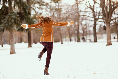 smiling modern 40 years old woman in brown hat and scarf outdoors in the city park in winter in sheepskin coat near snowy branches.の写真素材