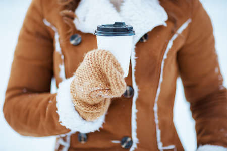 Full length portrait of smiling modern 40 years old woman with mittens in a knitted hat and sheepskin coat walking outdoors in the city park in winter.の写真素材