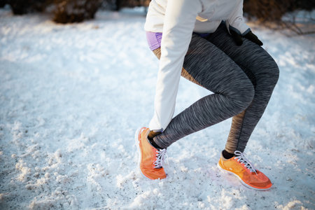 smiling fitness woman in white jacket with headphones outside in the city park in winter.