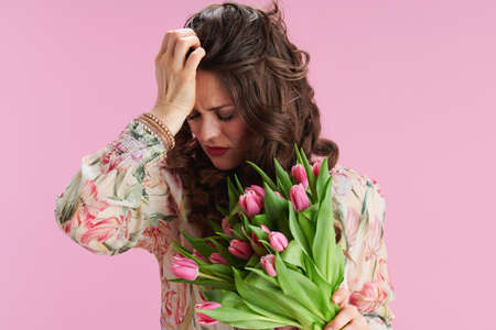 Portrait of stylish 40 years old woman in floral dress with glass of water isolated on pink.の写真素材