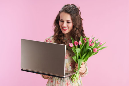 Portrait of stylish 40 years old woman in floral dress with glass of water isolated on pink.の写真素材