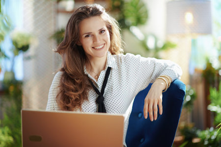 Green Home. smiling trendy woman with long wavy hair at modern home in sunny day using a smartphone.