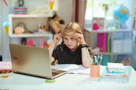 Portrait of happy modern school girl in gray shirt with tablet PC homeschooling at home in sunny day.の写真素材