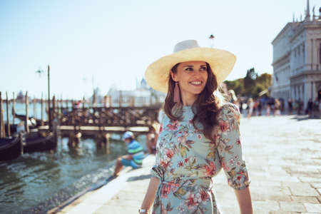 happy modern woman in floral dress with hat having walking tour on embankment in Venice, Italy.の写真素材