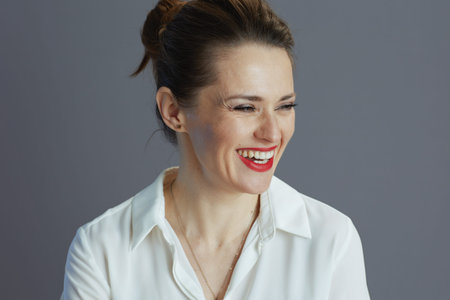 happy young female employee in white blouse against grey background.