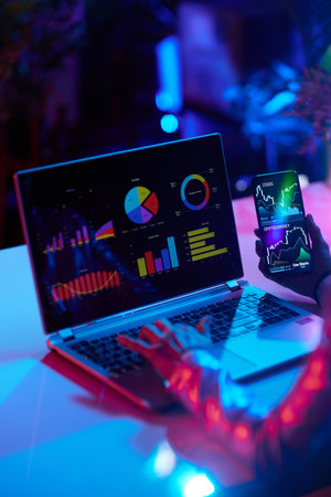 Seen from behind modern business woman with laptop and smartphone checking financial charts and trading online investment data in modern office.の写真素材