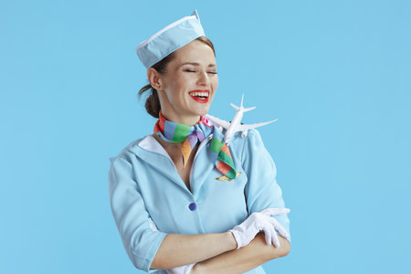 smiling stylish female air hostess against blue background in blue uniform with a little airplane.の写真素材