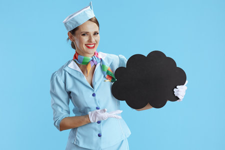 happy stylish air hostess woman isolated on blue background in blue uniform showing blank cloud shape board.の写真素材