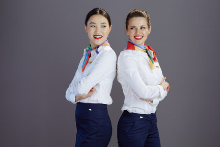 smiling stylish female air hostesses in blue skirt, white shirt and scarf against gray background.の写真素材