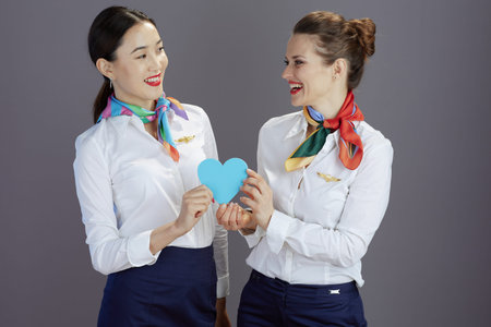 happy modern flight attendant women in blue skirt, white shirt and scarf with heart isolated on gray.の写真素材