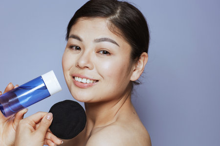 Portrait of young asian woman with makeup remover and black cotton pad on blue background.の写真素材