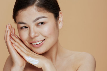 Portrait of modern Asian woman with hand cream on beige background.の写真素材