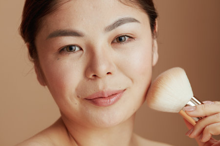 Portrait of modern Asian woman with makeup brush on beige background.の写真素材