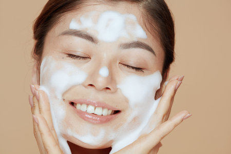 Portrait of modern Asian woman washing face against beige background.の写真素材