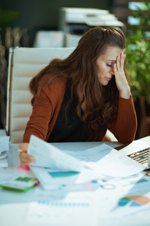 tired trendy small business owner woman working with documents in the modern green office.の写真素材