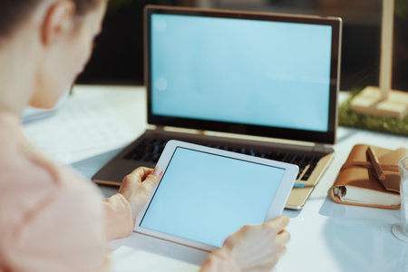 Seen from behind modern woman with laptop blank screen and tablet PC blank screen in modern office.