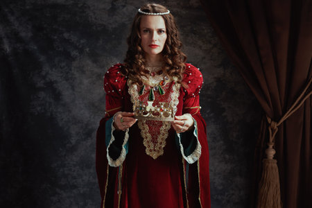 medieval queen in red dress with crown on dark gray background.の写真素材