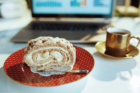 Mental health at work concept. Closeup on desk in modern office with piece of cake, cup of coffee and laptop.の写真素材