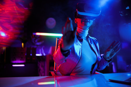 Neon metaverse futuristic concept. curious modern middle aged woman in virtual reality goggles in modern office.の写真素材