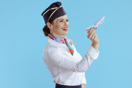 smiling modern flight attendant woman against blue background in uniform with a little airplane.の写真素材