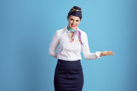 happy elegant flight attendant woman against blue background in uniform welcoming.の写真素材