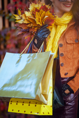 Hello October. smiling 40 years old woman in orange trench coat with shopping bags and autumn yellow leaves in the city.の写真素材