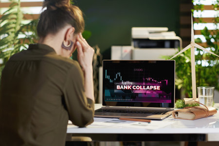 Seen from behind modern woman with laptop with bank collapse screen in modern office.の写真素材
