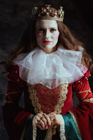 medieval queen in red dress with white collar and crown on dark gray background.の写真素材